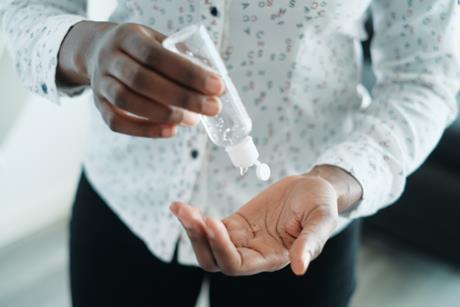 A person squeezing a plastic bottle of hand sanitizer into their palm