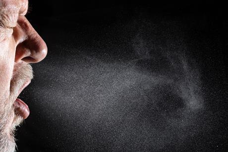 Close up of a man sneezing showing the droplets spreading from his nose and mouth
