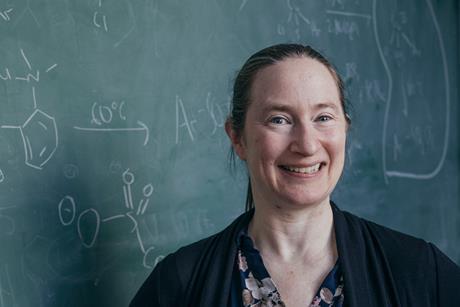 Melanie Sanford with a green chalkboard and chemistry symbols