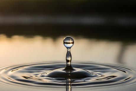 A single water droplet creates ripples on a serene lake surface at sunset