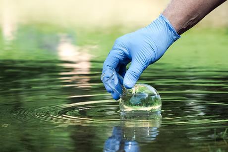Close up of a gloved hand collecting a water sample with a beaker