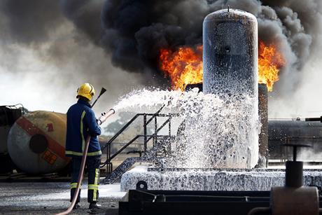 A firefighter sprays foam from a hose over a blaze on some chemical containers