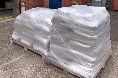 A man outside an industrial facility standing next to two pallets loaded with full sacks