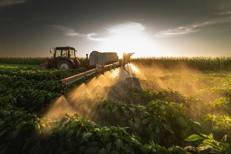 Tractor spraying glyphosate at sunset