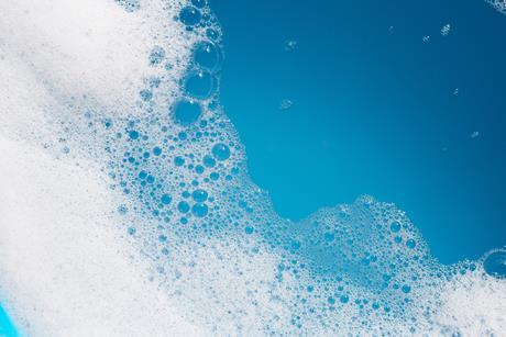 Detergent foam bubble on water with blue background.