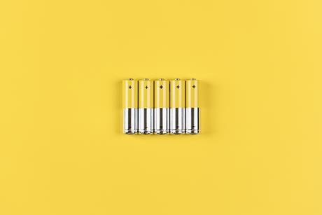 Photo of five grey-yellow alkaline AA batteries on a yellow background.