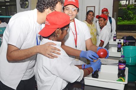 A scientist helps two visually impaired high school students perform a chemistry experiment with a bottle of fizzy drink and a balloon. The students are smiling as they feel the changes to the objects.