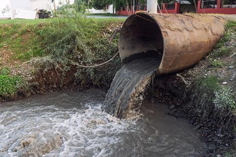 A sewage pipe empyting into a river near some buildings