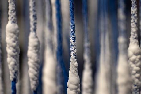 A close up of some blue string hanging vertically with small white crystals