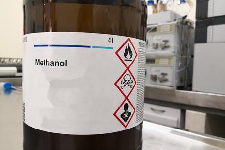 A bottle of methanol with hazard symbols warning it is flammable, toxic and health hazard on its label in a lab.