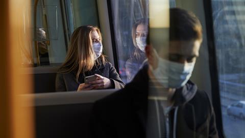 A woman sitting on a train wearing a medical mask
