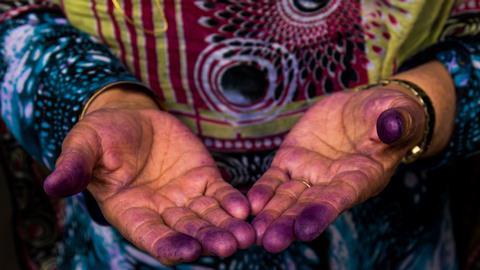 A Bandari woman showing her hands with indigo traces after sewing a traditional burqa mask
