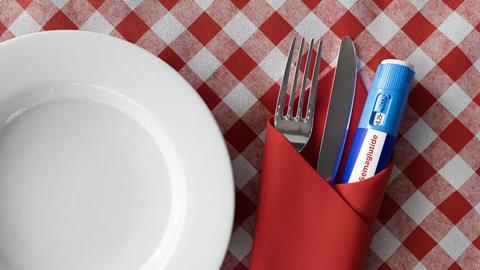 A semaglutide injecting 'pen' wrapped in a napkin with a knife and fork, on a red gingham tablecloth, next to a white plate