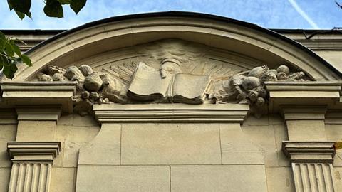 The top of an old building with a stone relief  of a hand holding an open book