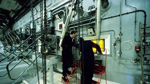 Technicians working a large piece of equipment with a window into a glowing furnace