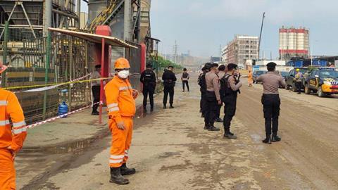 In Indonesia, uniformed police officers and workers in safety equipment at an industrial plant