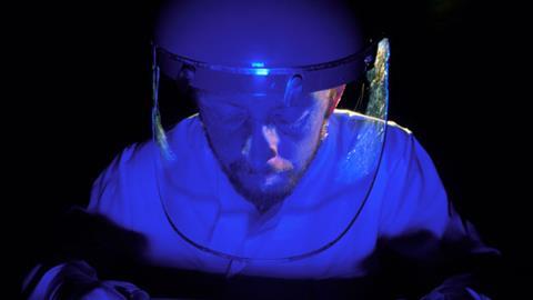 Man in protective clothing looking at fluorescing DNA slide