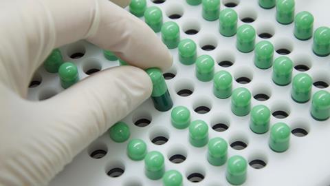Close-up image showing a gloved hand removing a green pill from a pill tray