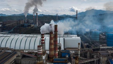 An image showing a hilly industrial area; multiple chimneys producing polluting gases can be seen