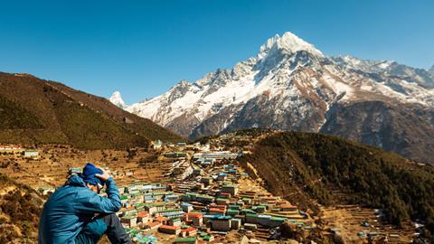 A man sits on a Nepalese mountainside with his head in his hands - apparently suffering from altitude sickness
