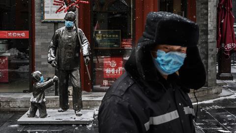 A protective mask is seen on statues outside a restaurant as a guard wearing a protective mask walks by in an empty and shuttered commercial street on February 5, 2020 in Beijing, China