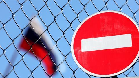 Access denied flag in front of fence with Russian flag blurred in the background behind the fence