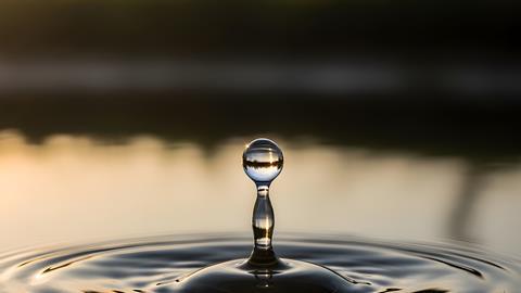 A single water droplet creates ripples on a serene lake surface at sunset