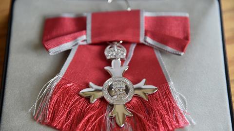 A silver MBE medal on a red bow