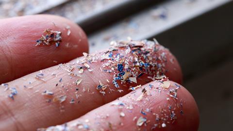 A closeup photo of fingers with an array of tiny colourful plastic particles stuck to it