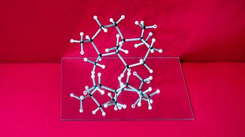 A photo of a molecular model of drimane, a bicyclic natural product, sitting on top of a mirror on a velvet red background