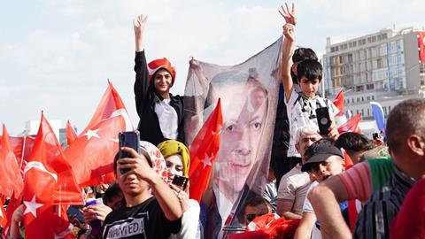 A crowd at a political rally in Turkey waving Turkish flags and a banner with the face of President Erdogan