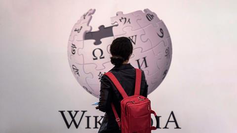 An image showing a woman standing in front of Wikipedia sign