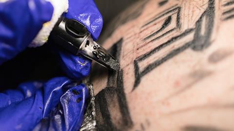 An image showing a closeup of the hand of a tattoo artist using a pen with black tattoo ink