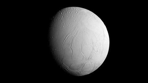 An image of Enceladus, a cratered white sphere hanging in the dark of space