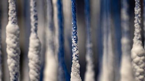 A close up of some blue string hanging vertically with small white crystals