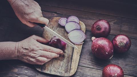 Chopping onions on a wooden board with a ceramic knife