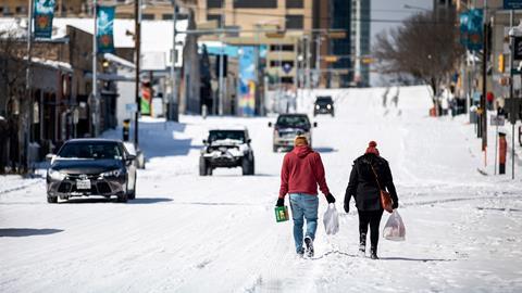 A photo of two people walking along a snow covered city road, carrying shopping bags