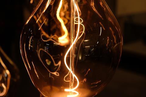 Close up of designer light installation, showing see through glass lamp and light bulb with filament illuminated.
