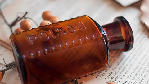 Image of a brown poison bottle lying on a book and notes, surrounded by poison pills