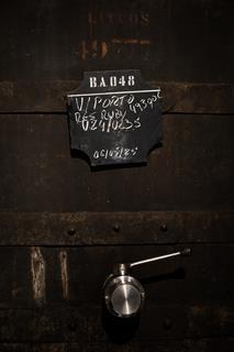 Close-up photo of a barrel with a modern steel tap and a blackboard label with numbers and dates on