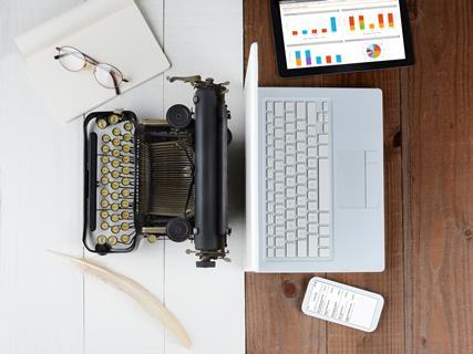 Image shows a laptop and old fashioned typewriter plus various desk items