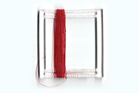 A photo of red thread wound around a small plastic square
