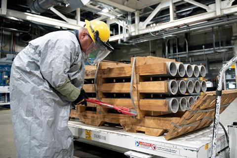 A man wearing protective clothing uses bolt cutters to open a crate of missiles in a warehouse