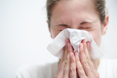 Woman blowing nose and sneezing into tissue