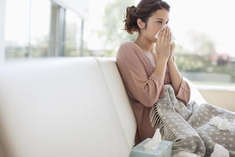 Woman on sofa blowing nose into tissue