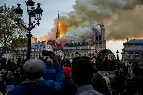 An image showing people watch the landmark Notre-Dame Cathedral burning in central Paris on April 15, 2019