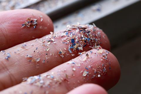 A closeup photo of fingers with an array of tiny colourful plastic particles stuck to it