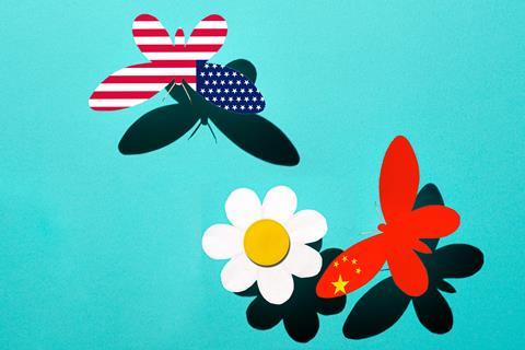 Two butterflies made of paper, one with an American flag on its wings the other with the Chinese flag, approach a paper flower.
