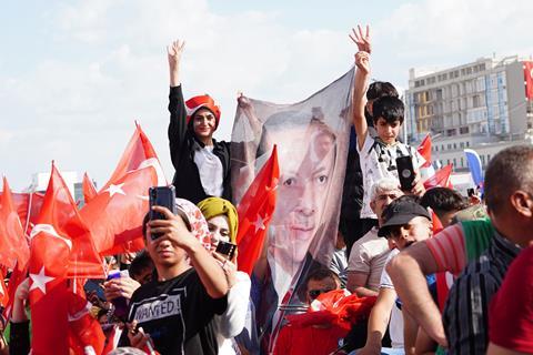 A crowd at a political rally in Turkey waving Turkish flags and a banner with the face of President Erdogan