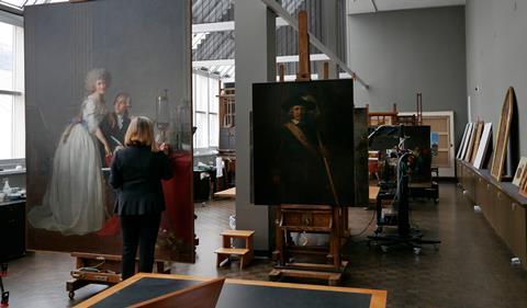 An art conservator working on a painting of a man and woman in 18th century dress